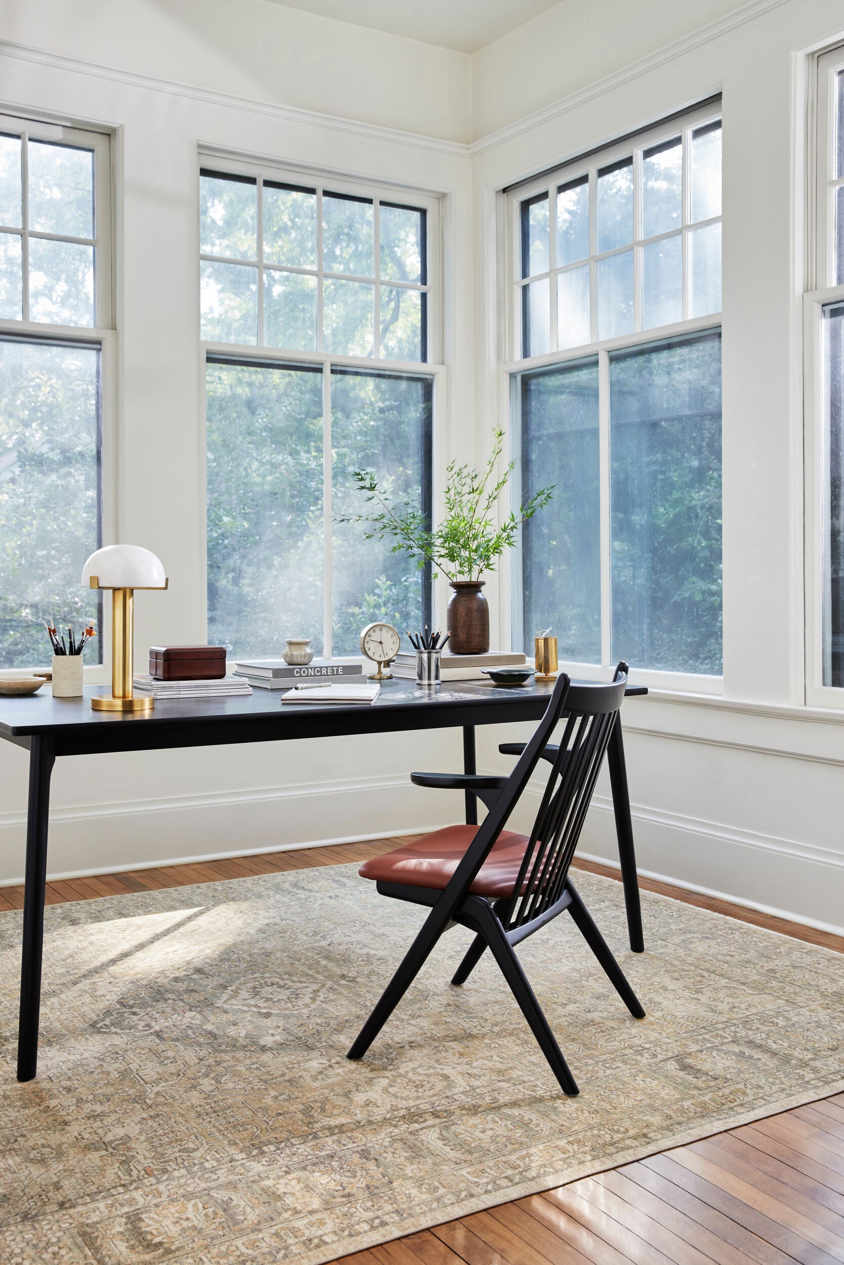 Black dining armchair with brown faux leather seat placed at a sleek black desk in a bright home office.