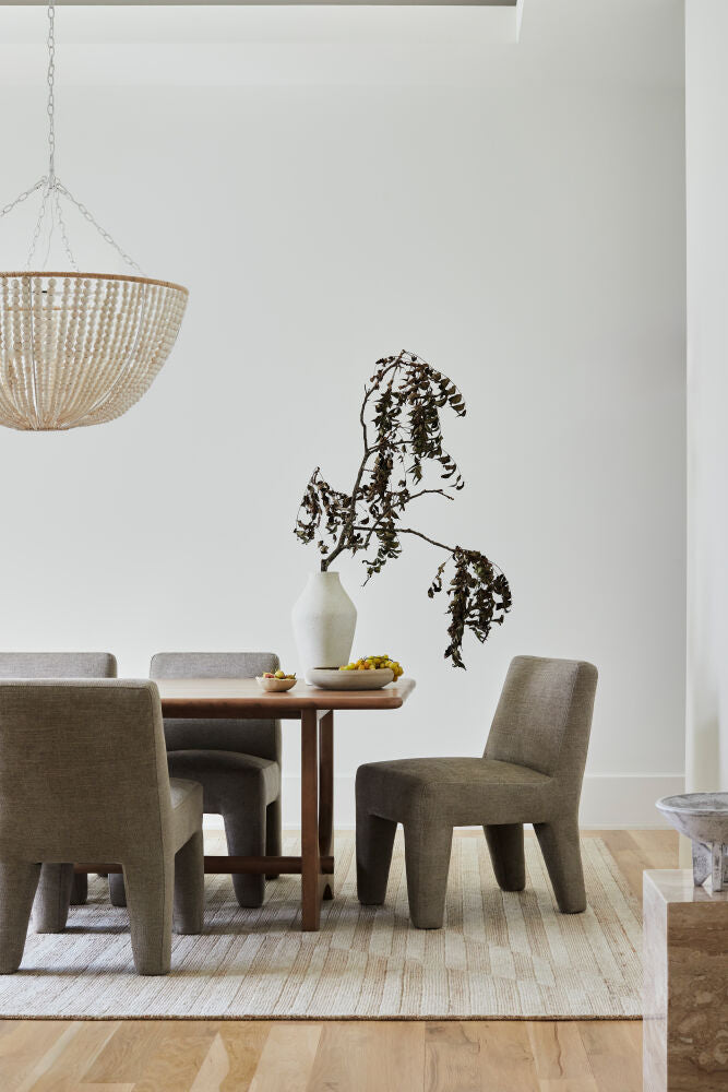 Scandinavian-style mango wood dining table with gray upholstered chairs, a neutral rug, and a beaded chandelier.