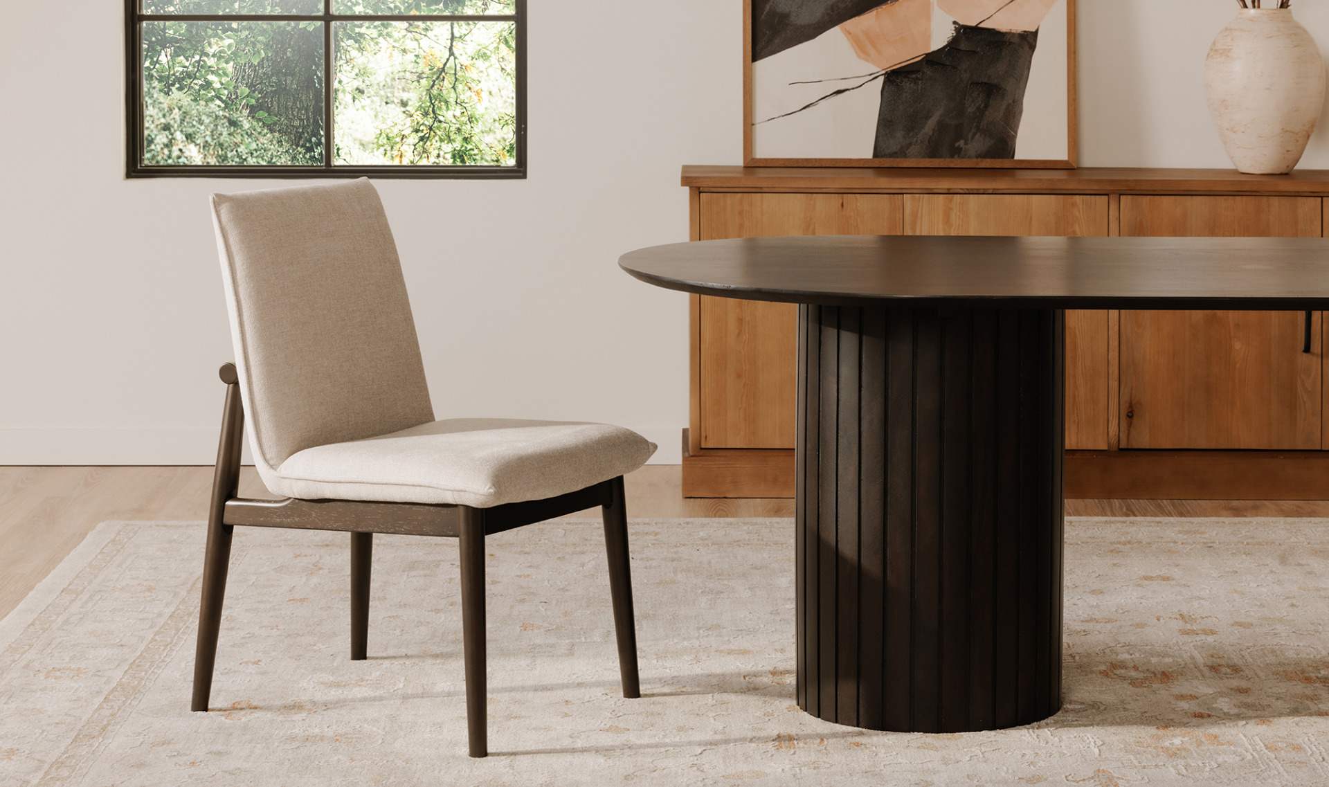Beige dining chair next to the Povera Black Dining Table with ribbed pillars in a minimalist room.