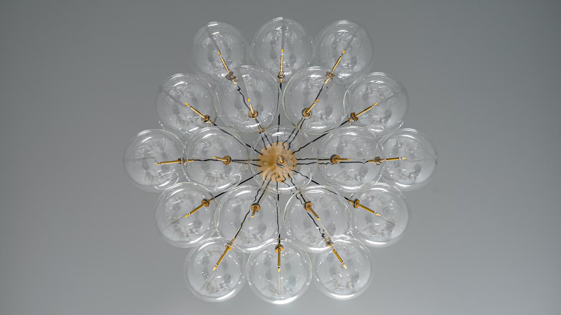 A bottom view of a cluster chandelier with clear glass globes, brass hub, and black cords.