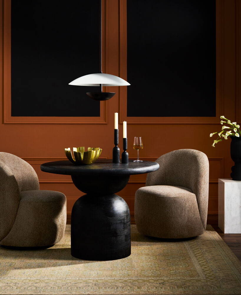 Modern dining setup with a black sculptural table, two light brown upholstered chairs, and a pendant light.