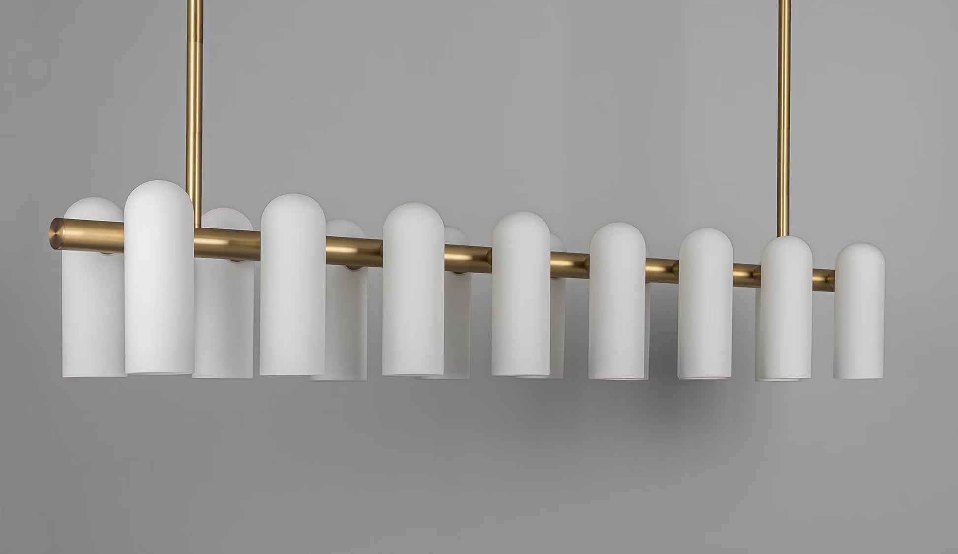 Oversized brass linear chandelier with frosted cylindrical shades in a contemporary style.