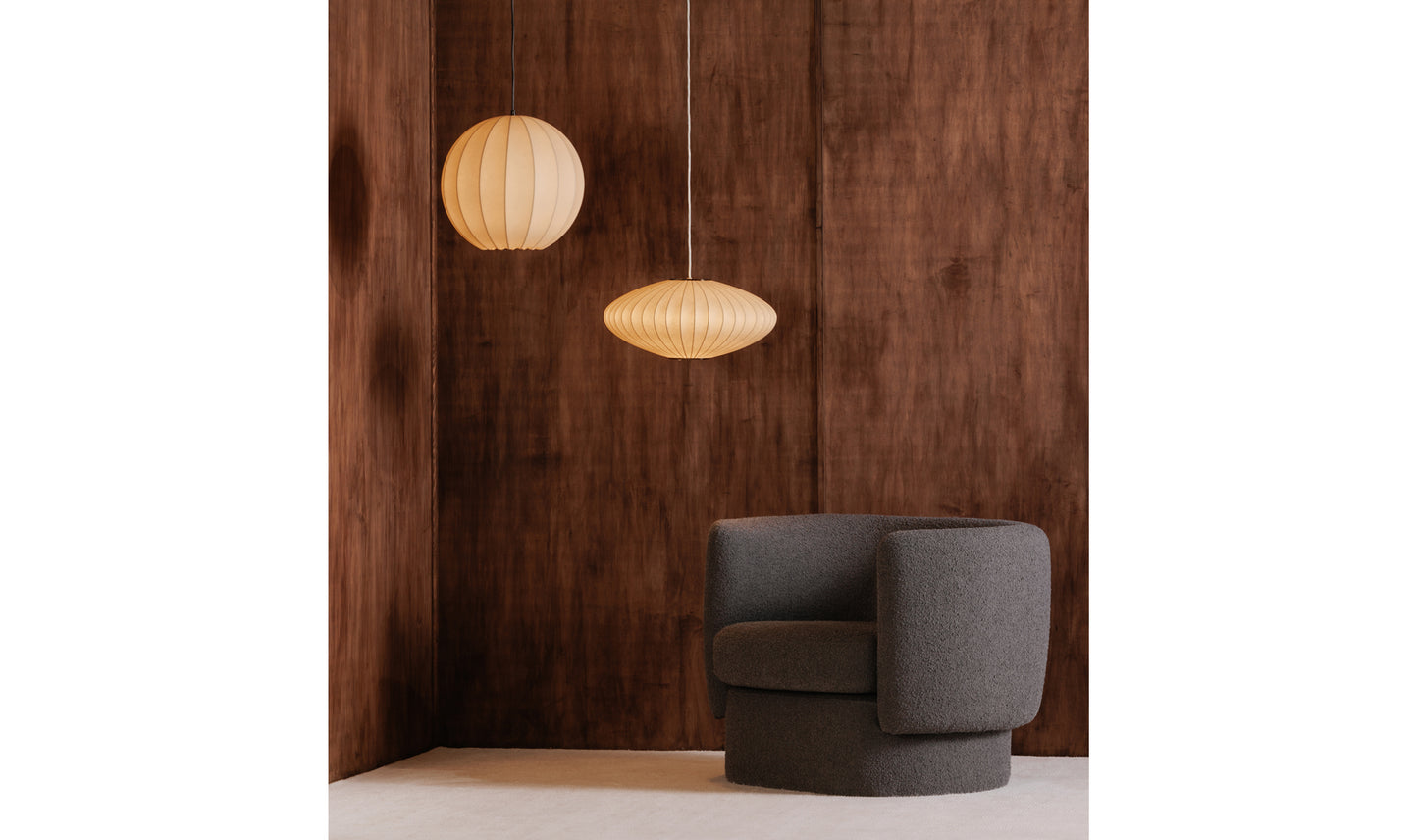 Lys white pendant light in a modern living room with dark wood walls and a contemporary grey chair