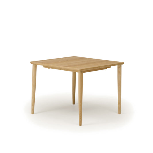Japandi-style square extension dining table in natural wood with smooth veneer top and tapered legs.