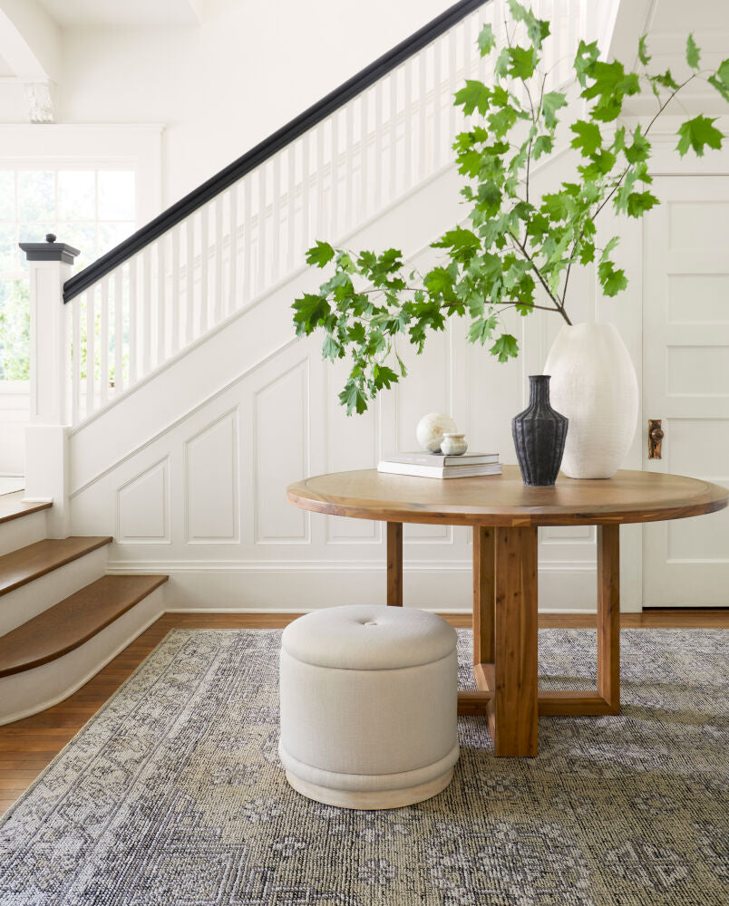 Minimalist Acacia dining table with a beige ottoman, styled with neutral decor on a patterned rug.