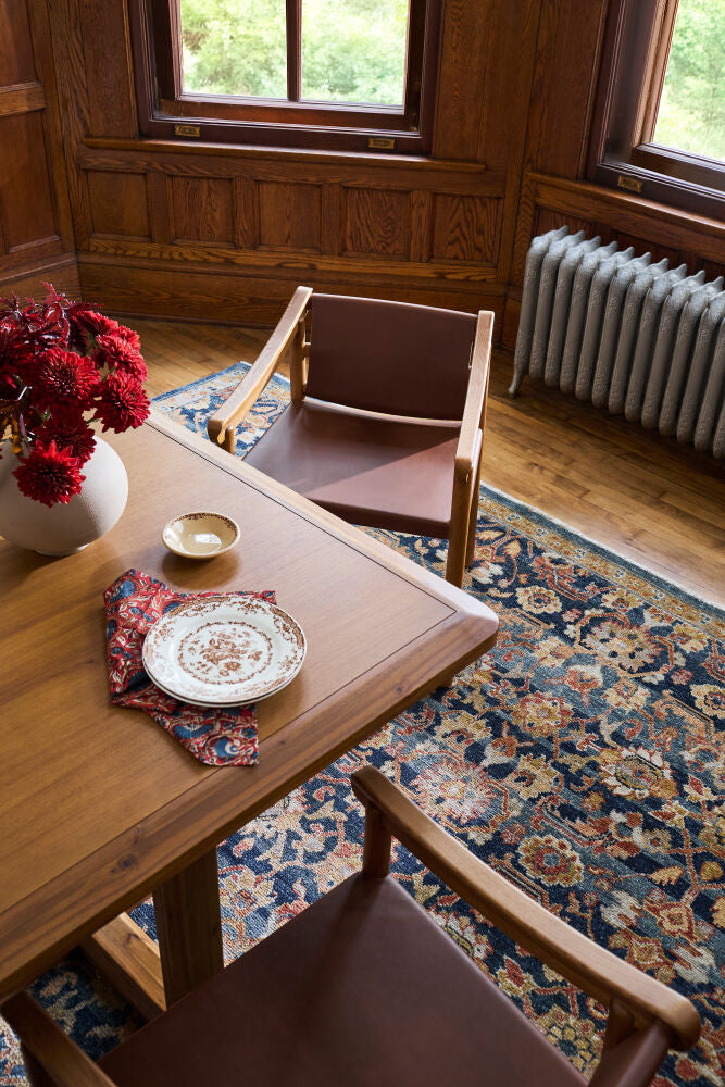 Wood dining table with a leather armchair, vintage rug, and elegant tableware in a warm, classic setting.