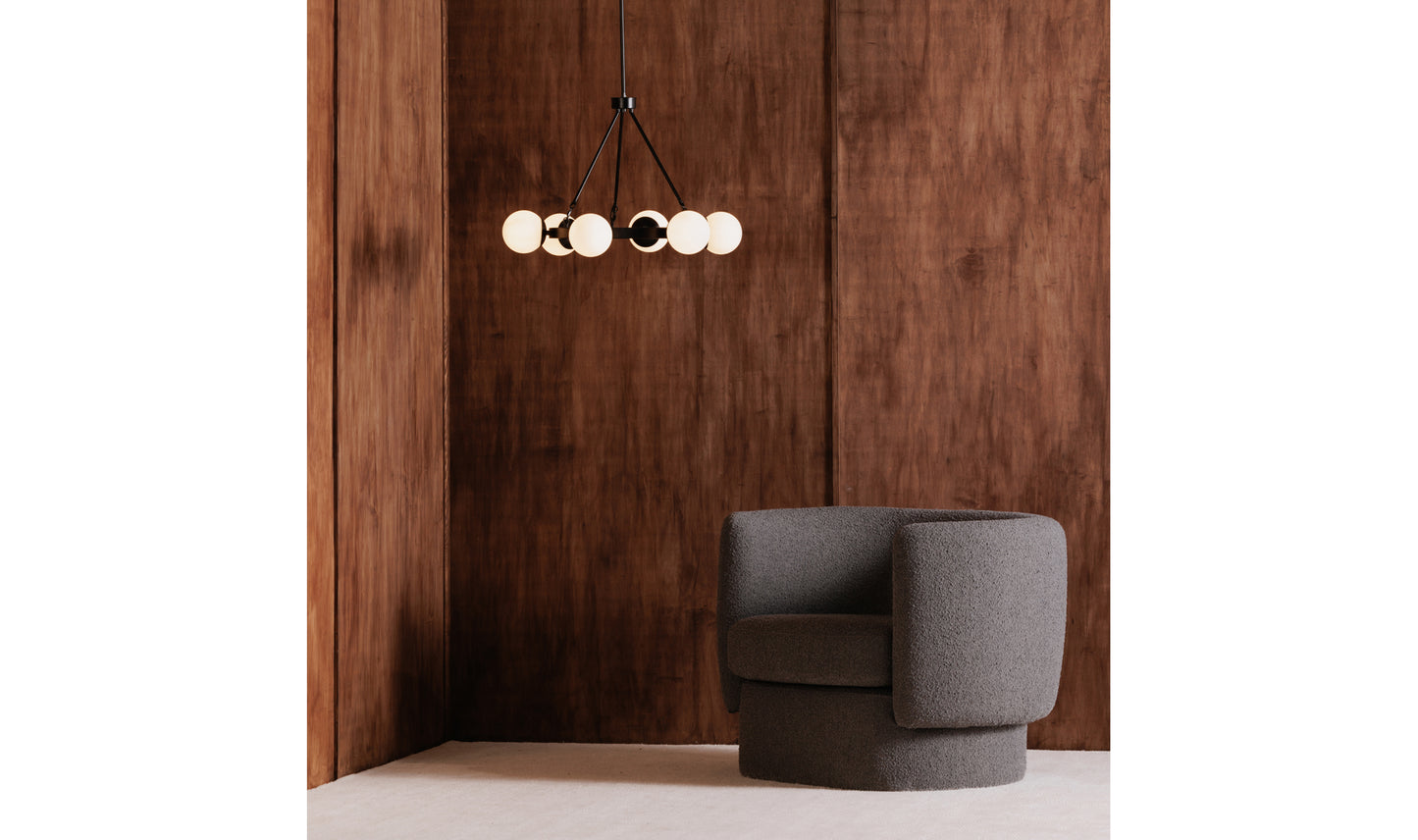 Oaha black pendant light in a cozy living room with dark wood walls and a grey accent chair