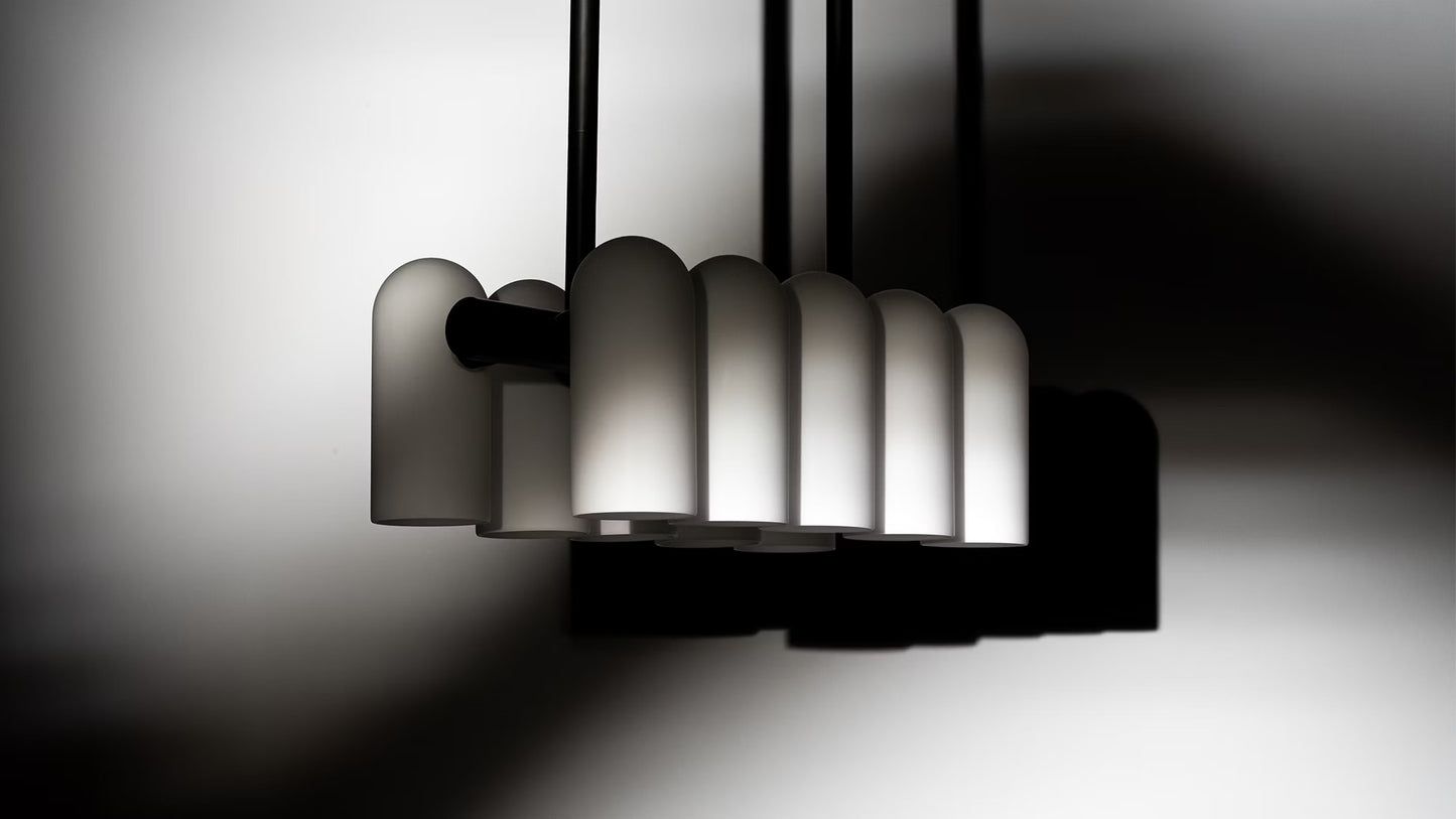 Contemporary black and white chandelier illuminated with soft lighting against a gradient background.