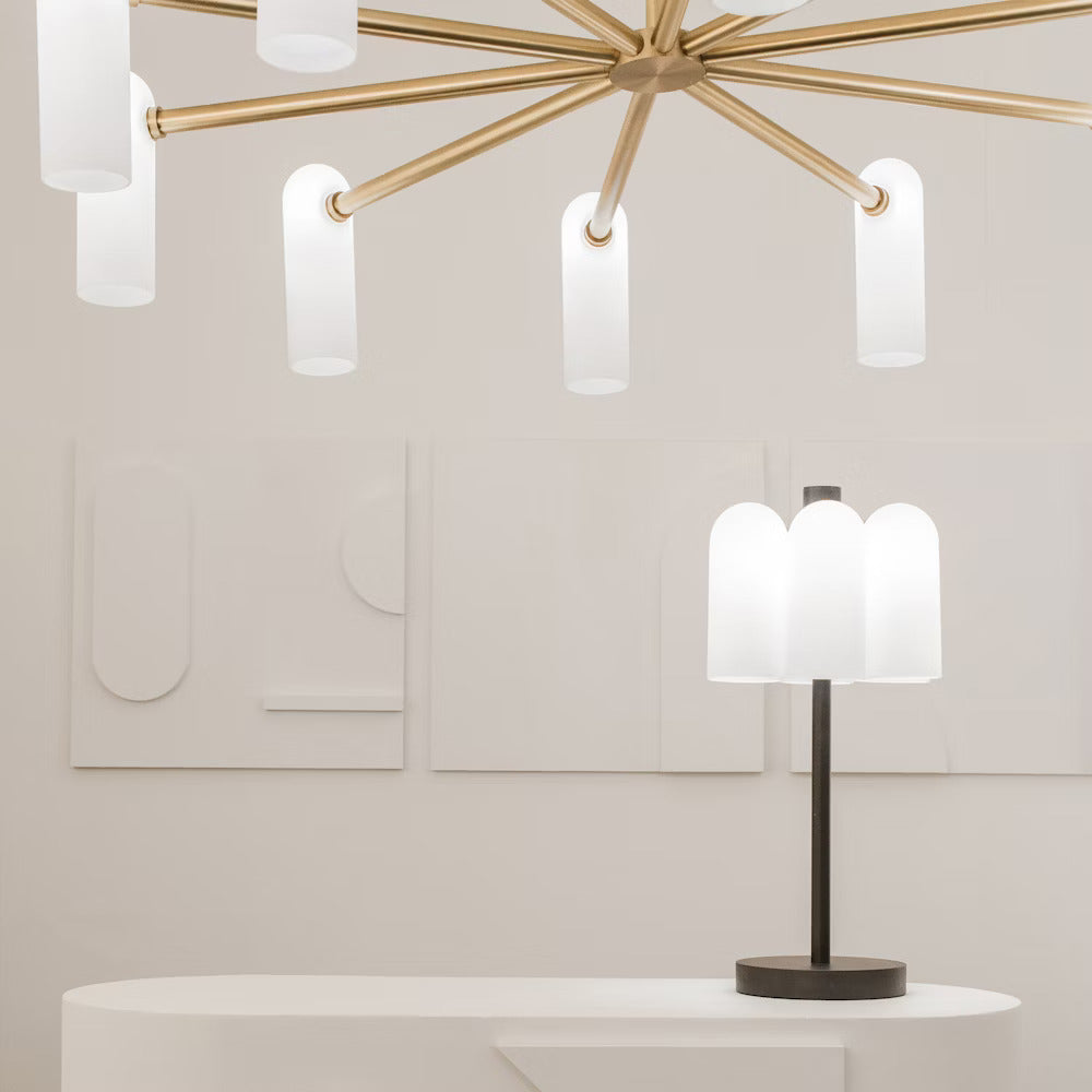 Brass chandelier and matching table lamp, both with white opal glass shades in a modern setting.