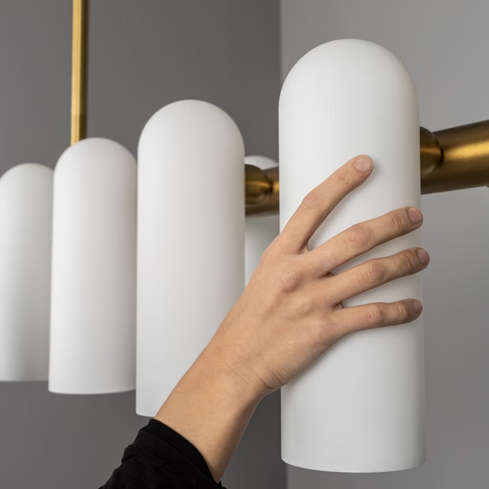 Hand touching a frosted glass shade, showcasing the craftsmanship of the chandelier design.
