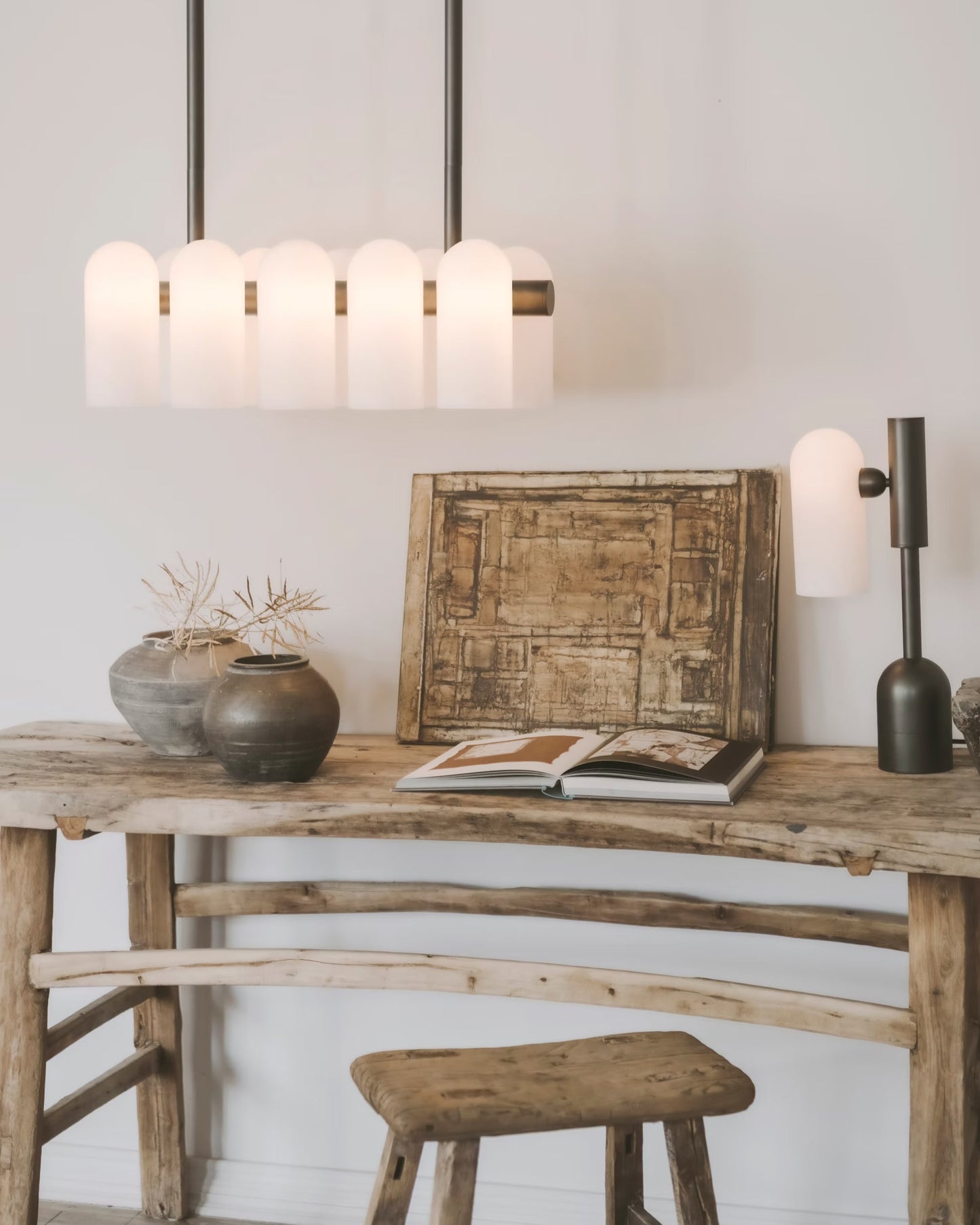 Linear chandelier with frosted glass shades suspended over a rustic wooden desk.