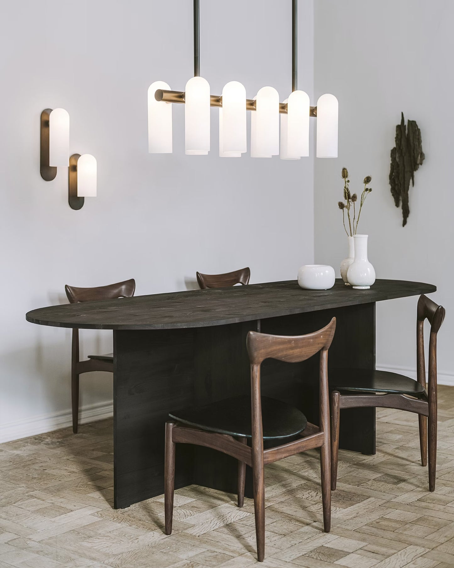 Elegant dining room setup featuring a small brass linear chandelier and matching wall sconces.