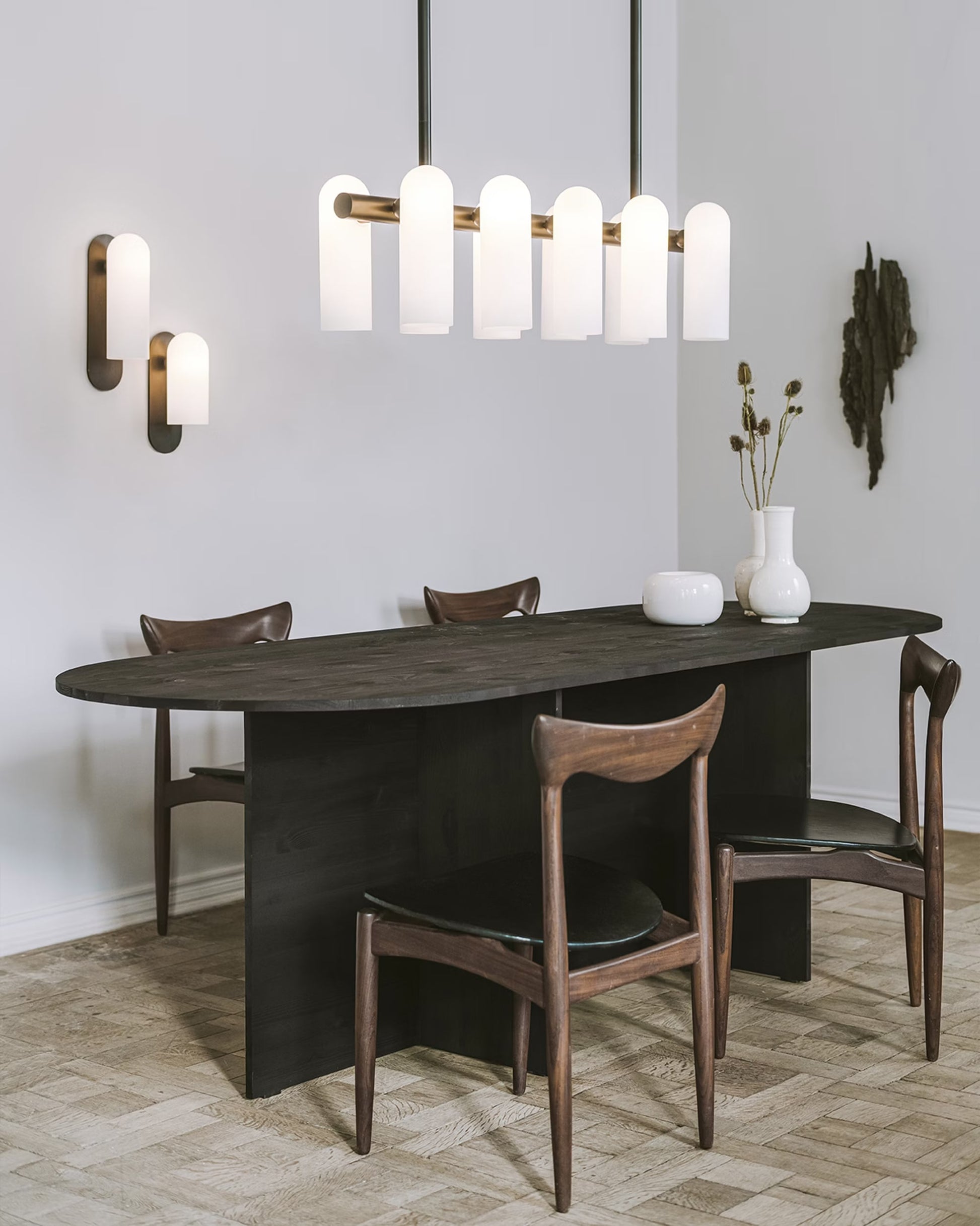 Elegant dining room setup featuring a small brass linear chandelier and matching wall sconces.
