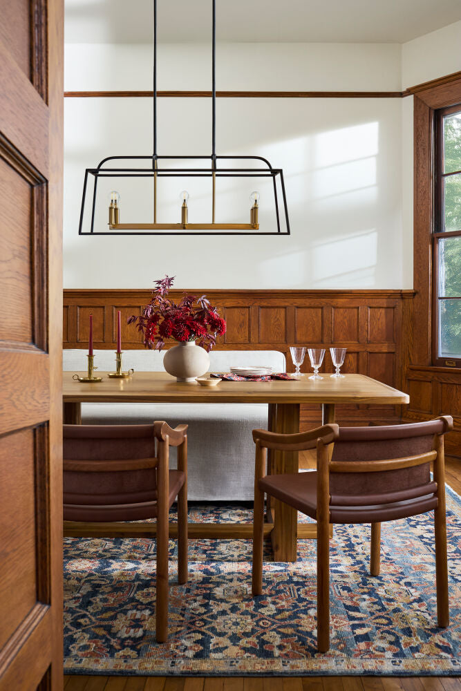 Wooden dining table with leather armchairs, a vintage rug, and elegant tableware in a warm setting.