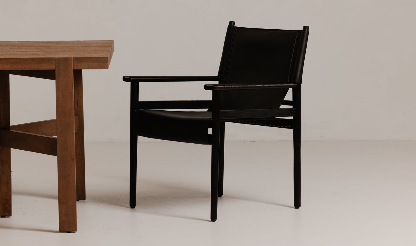 The Remy Black Leather Dining Chair placed next to a wooden dining table in a room setting