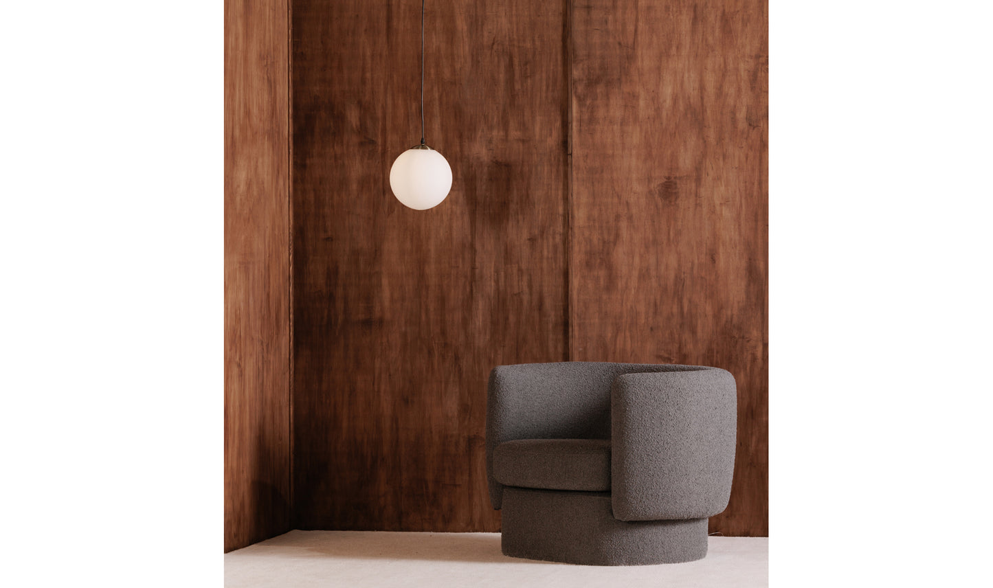 Sol pendant light hanging in a cozy living room with dark wood walls and a modern grey chair.