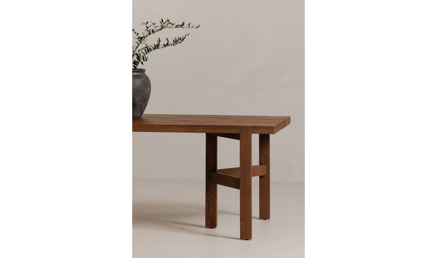 A close-up side view of the Workshop modern wooden dining table's corner, showing its clean-lined mango wood design and rustic brown finish,