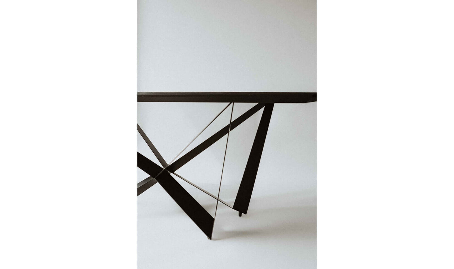 Close-up of the Brolio Dining Table’s sculptural triangular iron legs and dark mango wood tabletop