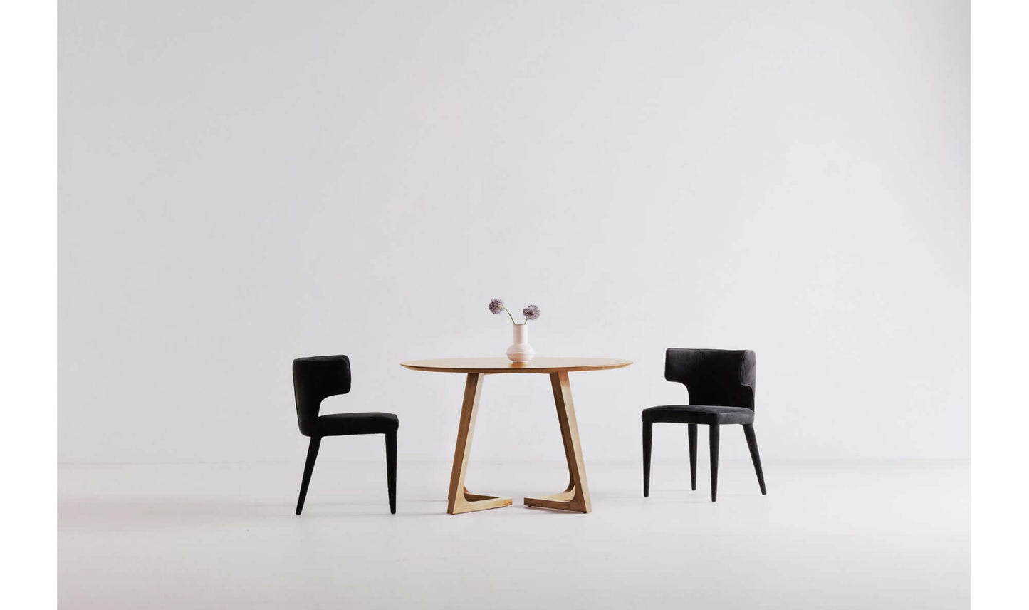 Godenza Round Oak Dining Table with two black chairs in a minimalistic dining room.