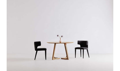 Godenza Round Oak Dining Table with two black chairs in a minimalistic dining room.