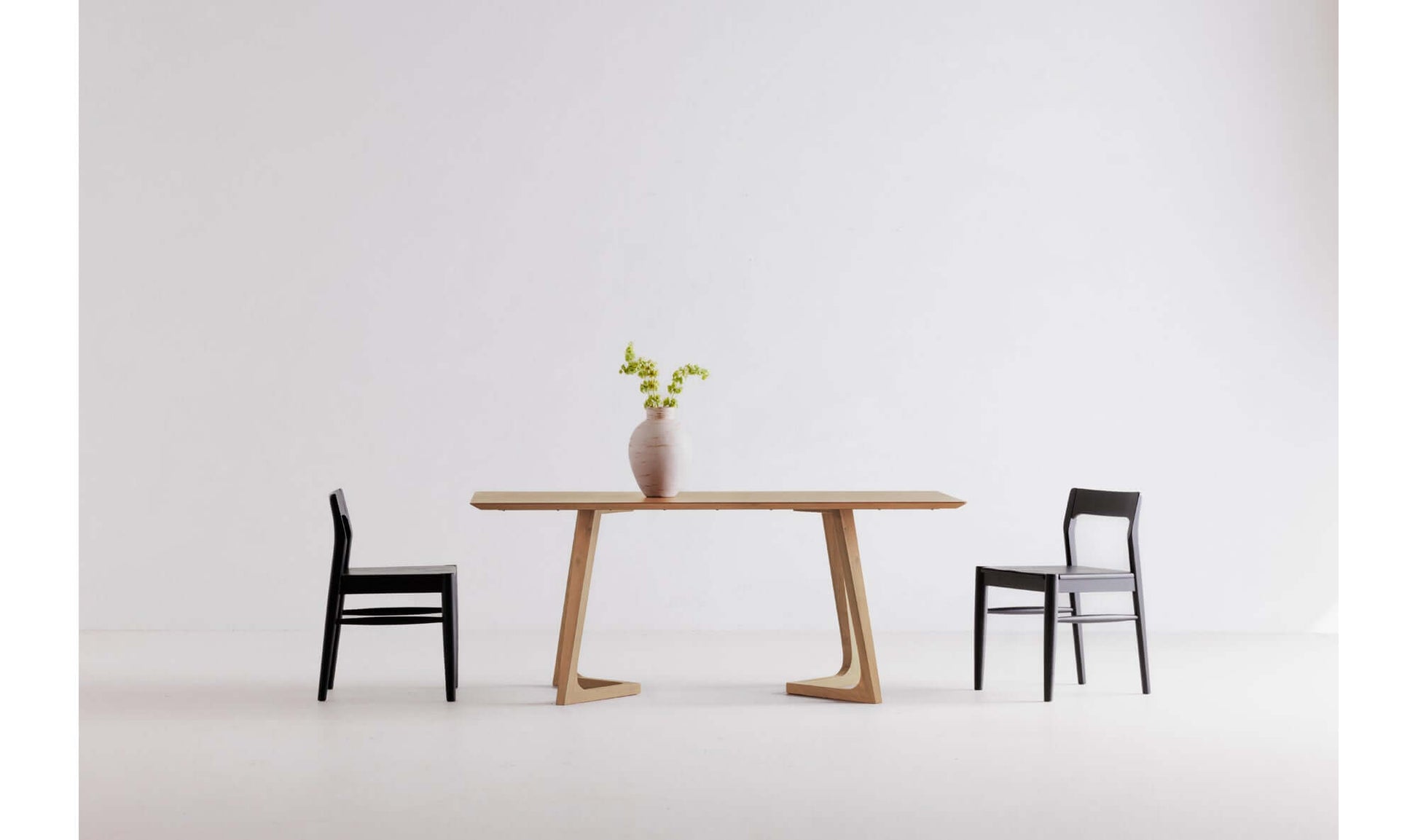 Minimalist dining room setup featuring the Godenza Oak Rectangular Dining Table with a vase centerpiece and two black chairs.