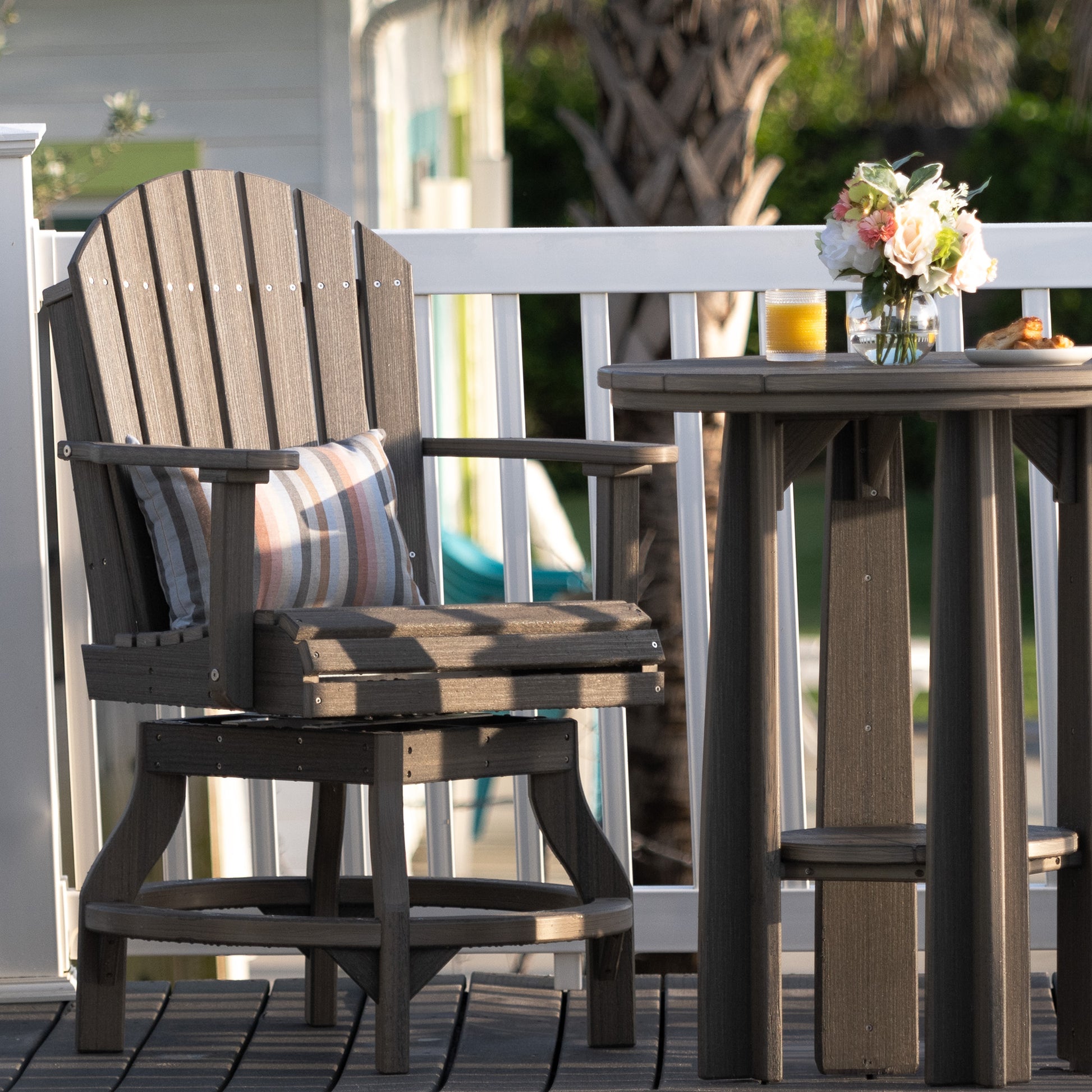 Coastal gray Adirondack counter swivel chair on a patio with a table and decorative pillow.