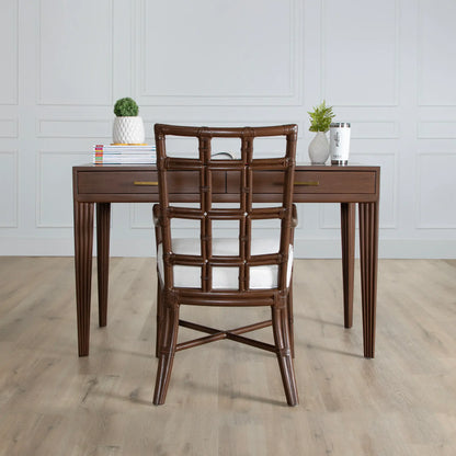 Full view of a brown rattan chair with a square-pattern backrest, placed in front of a wooden desk in a minimalist room setting.