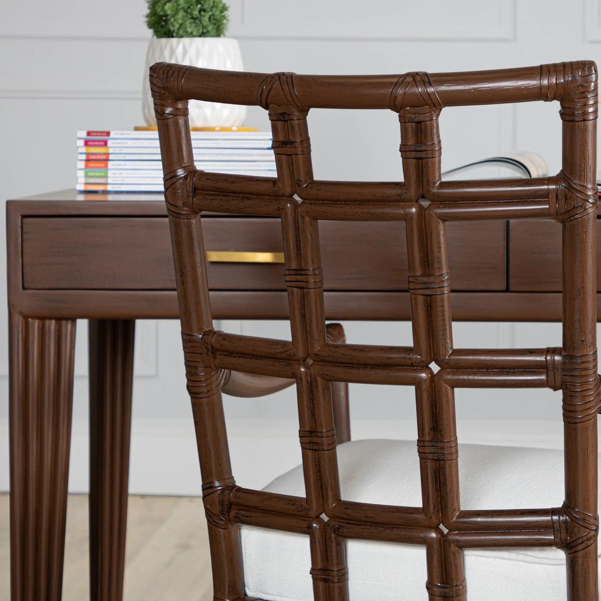 Close-up of a brown rattan chair's backrest, showcasing its square-pattern design, positioned in front of a wooden desk.