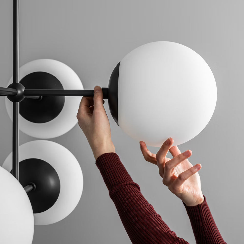 Hand adjusting a handblown opal matte glass globe on the Armstrong Linear Chandelier with black frame.