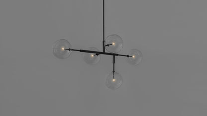 Black gunmetal chandelier with five glass globes, illuminated against a gray wall.