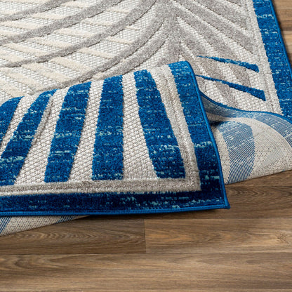 Corner fold detail of a blue and gray palm leaf rug showcasing its durable edge binding and polypropylene material.