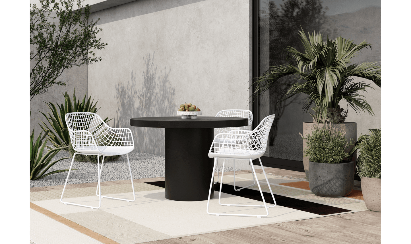 Cassius round outdoor dining table set in a stylish patio with white chairs and modern decor.