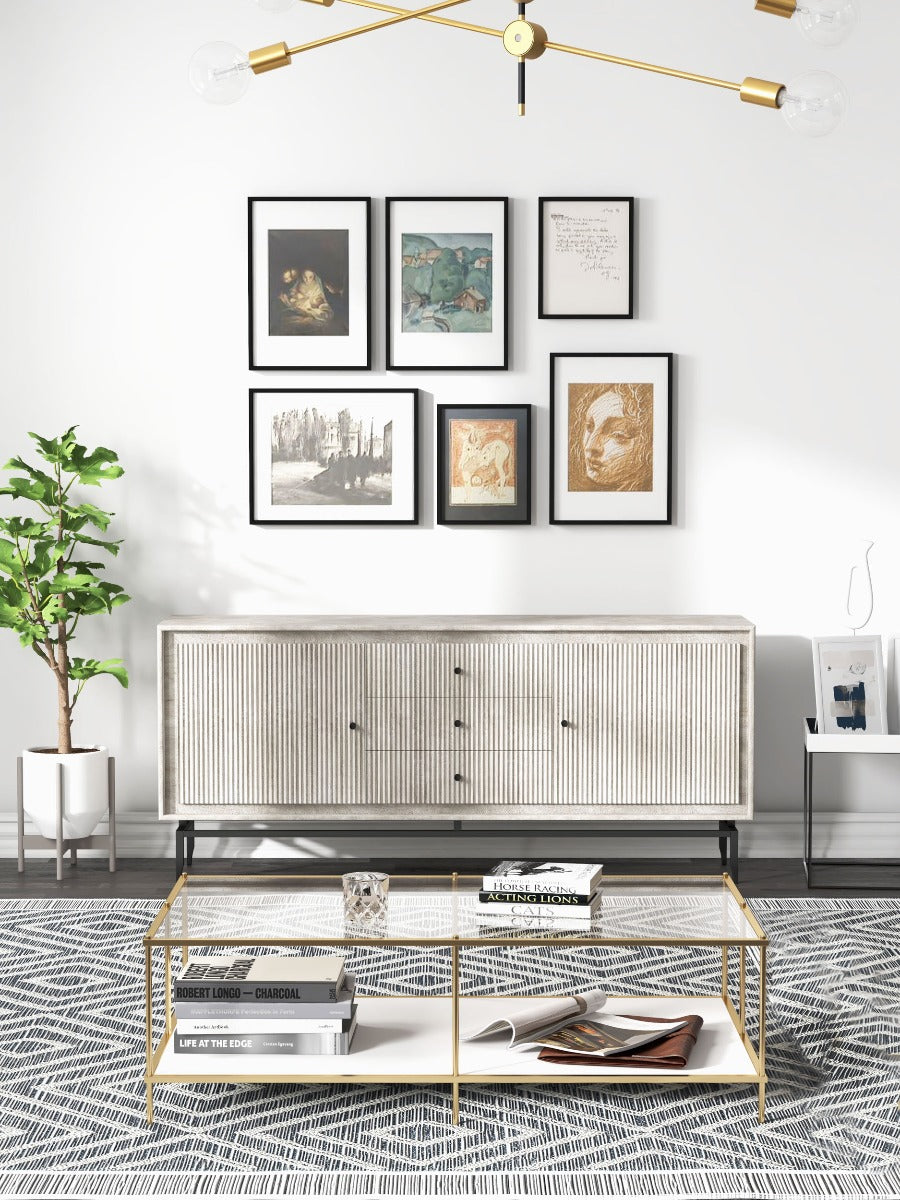 Grey sideboard under a gallery wall with art and greenery, featuring fluted doors and a sleek design.