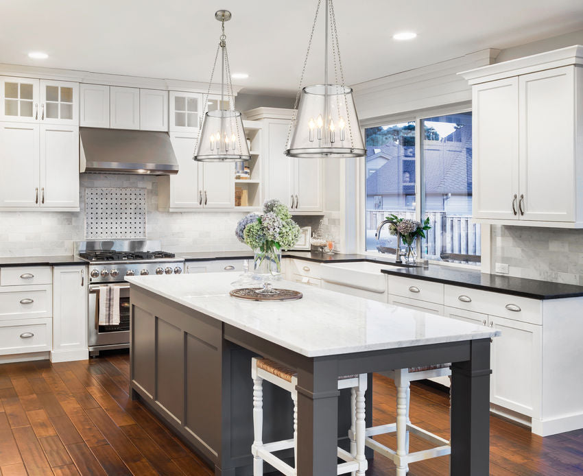 Pair of brushed nickel four-light pendants above modern kitchen island.