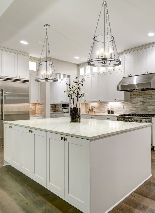 Polished nickel four-light pendants in bright white kitchen above marble island.