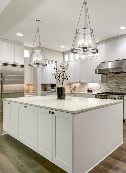 Polished nickel four-light pendants in bright white kitchen above marble island.