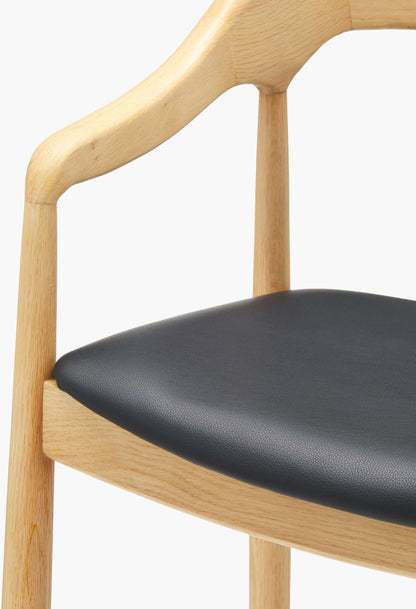 Close-up view of the Kisco Natural Bar Stool seat edge, featuring black faux leather upholstery and smooth natural wood finish.