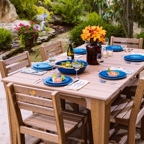 LuxCraft Island Dining Table in an outdoor setting, surrounded by dining chairs, set for a meal with blue plates and flowers