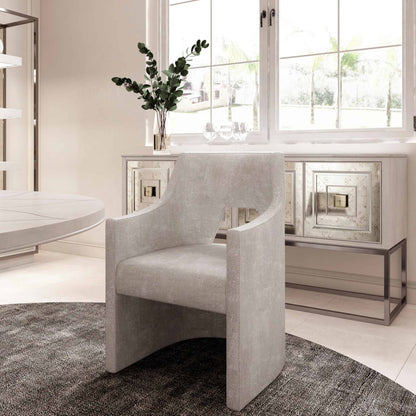 Grey upholstered dining armchair in front of a large window, paired with mirrored cabinets in a modern dining room.