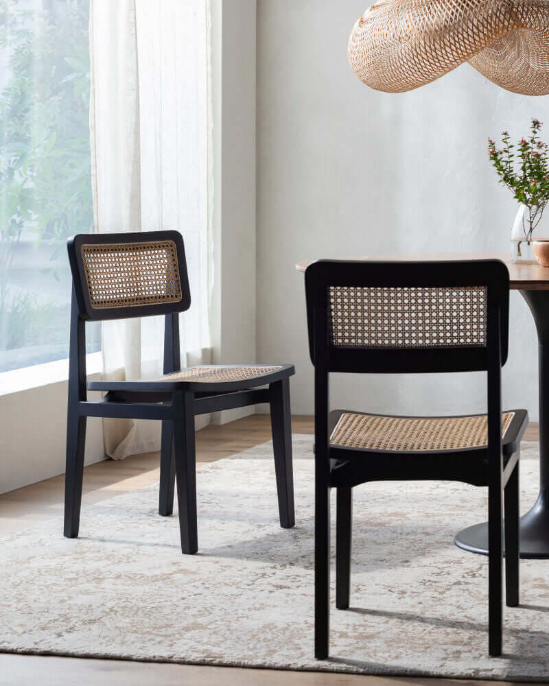 Two Surya Arxan modern rattan dining chairs in black finish in a stylish dining room setting with natural light and a woven pendant light.