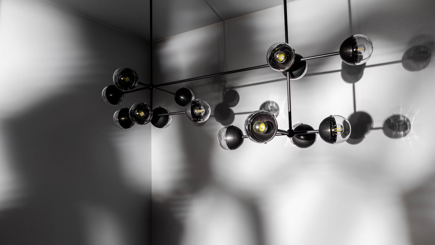 Molecule Linear Chandelier casting shadows on a minimalist gray wall, highlighting its sleek design.