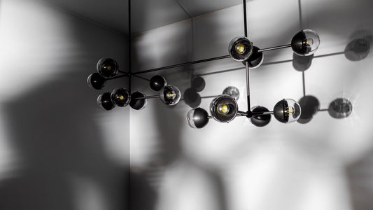 Molecule Linear Chandelier casting shadows on a minimalist gray wall, highlighting its sleek design.