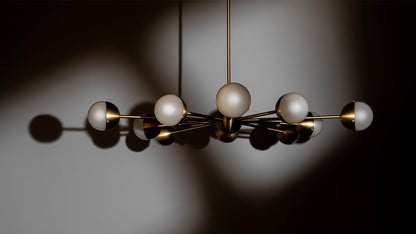 Frosted globe Molecule Spark Round 10 Chandelier with brass finish, casting soft shadows in dim light.