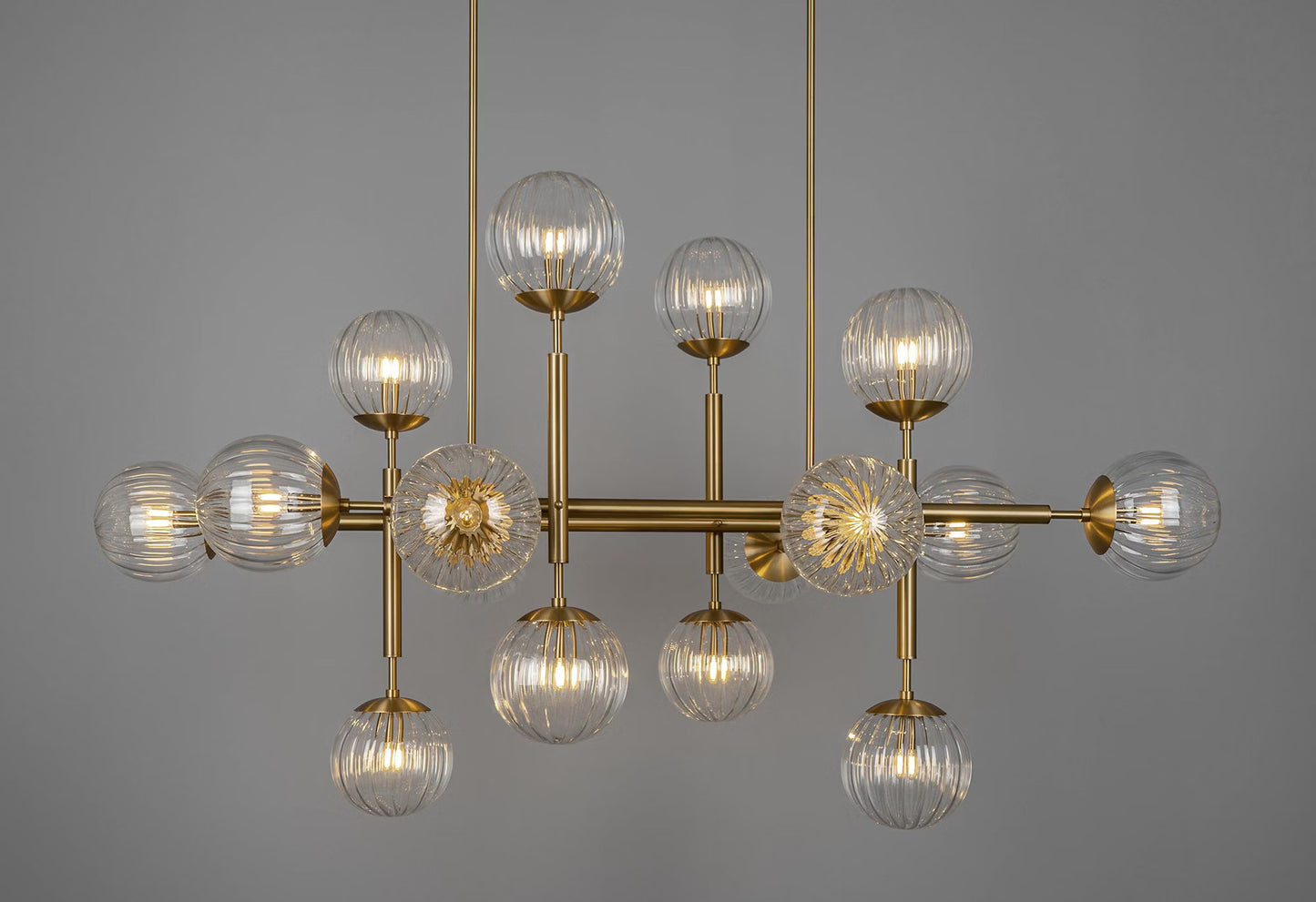 Luxurious brass linear chandelier with transparent ribbon glass globes, illuminated beautifully.