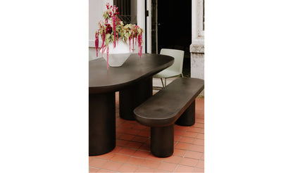 Rocca black concrete dining table with twin pillar base and oval top, set in an outdoor patio.