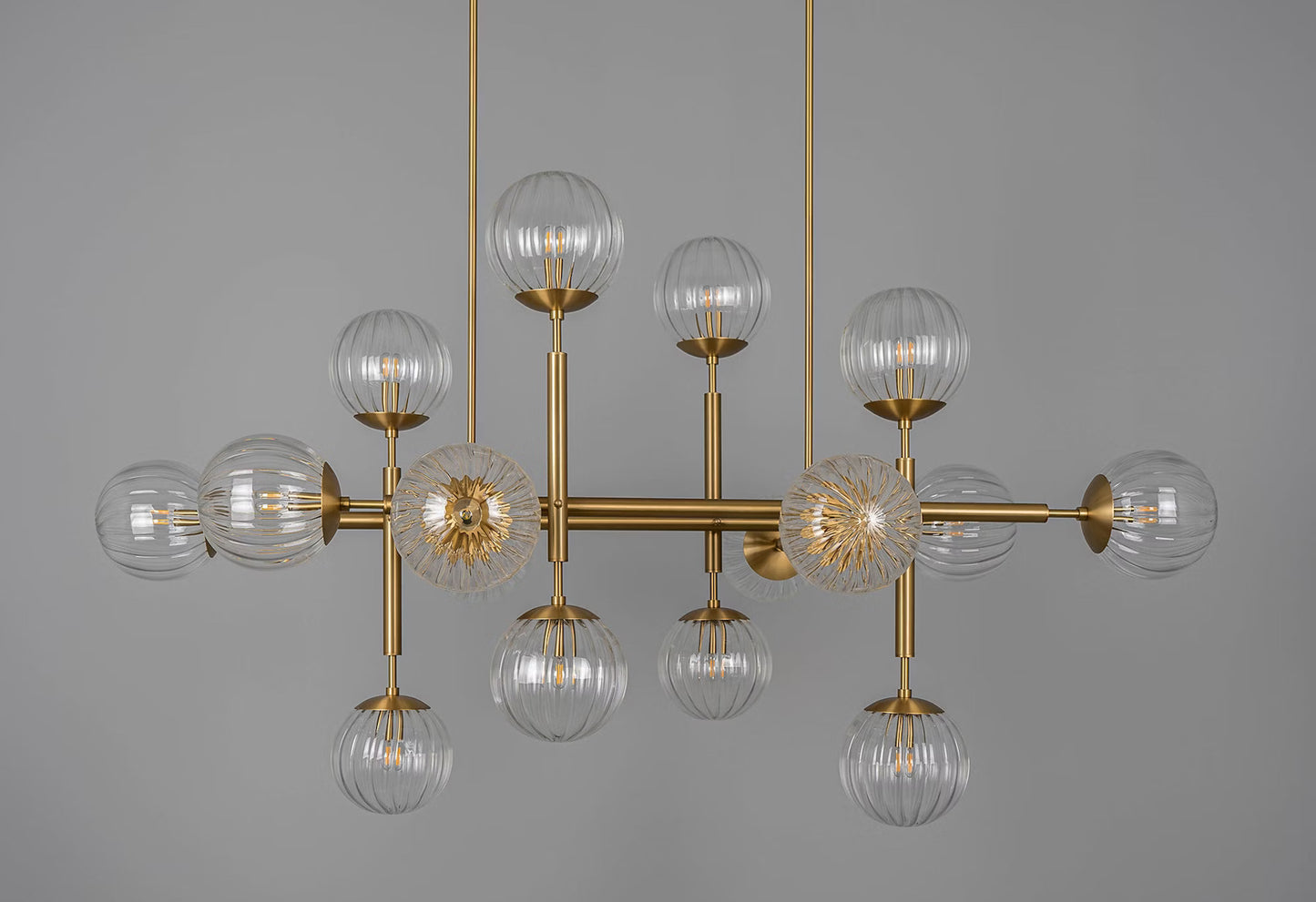 Luxurious linear chandelier with transparent ribbon glass globes and brass finish.